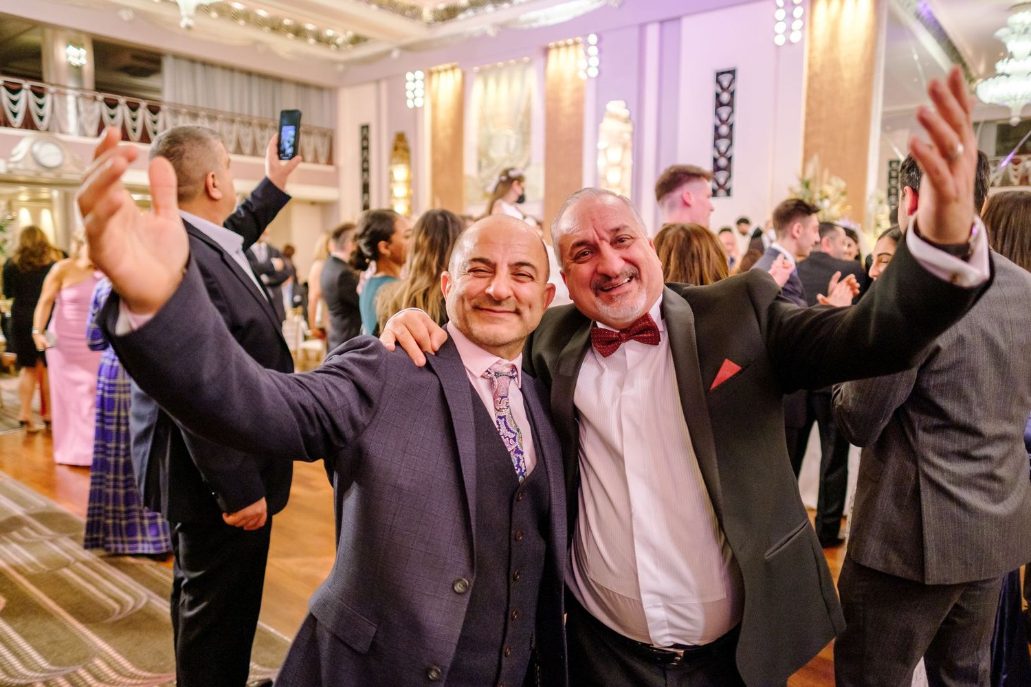 Wedding party and guests celebrating with raised arms in an elegant reception venue.