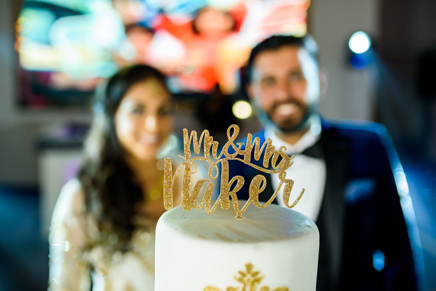 Wedding cake topped with Mr & Mrs decoration at an illuminated reception.