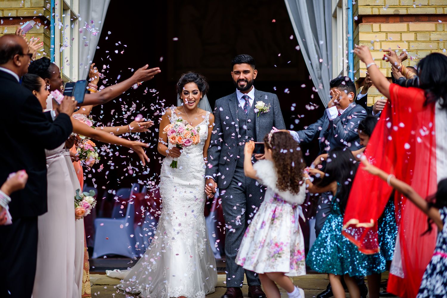 Joyful wedding celebration with confetti being thrown outside a brick building entrance.