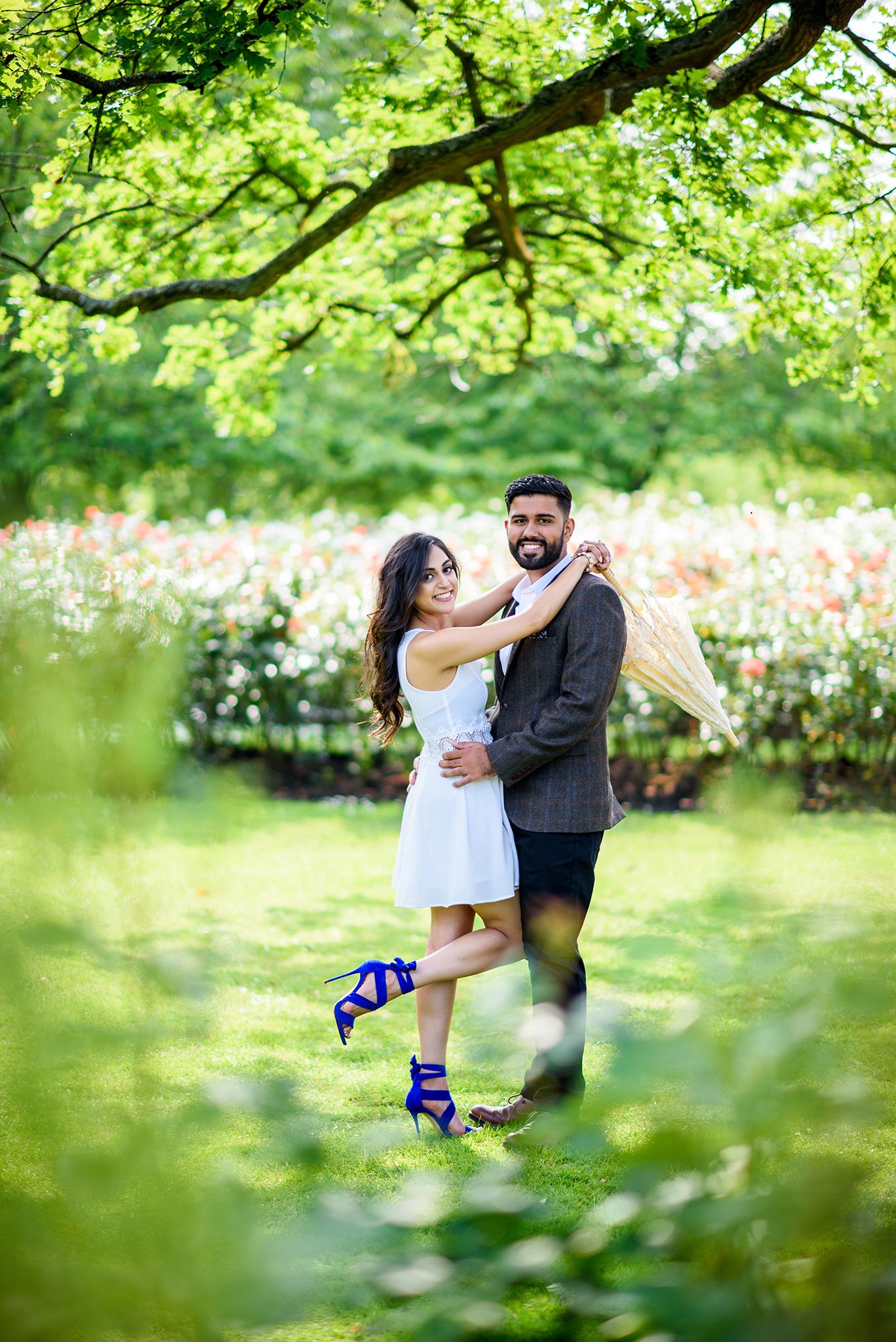 Romantic couple embraces under lush green tree branches in a garden setting.