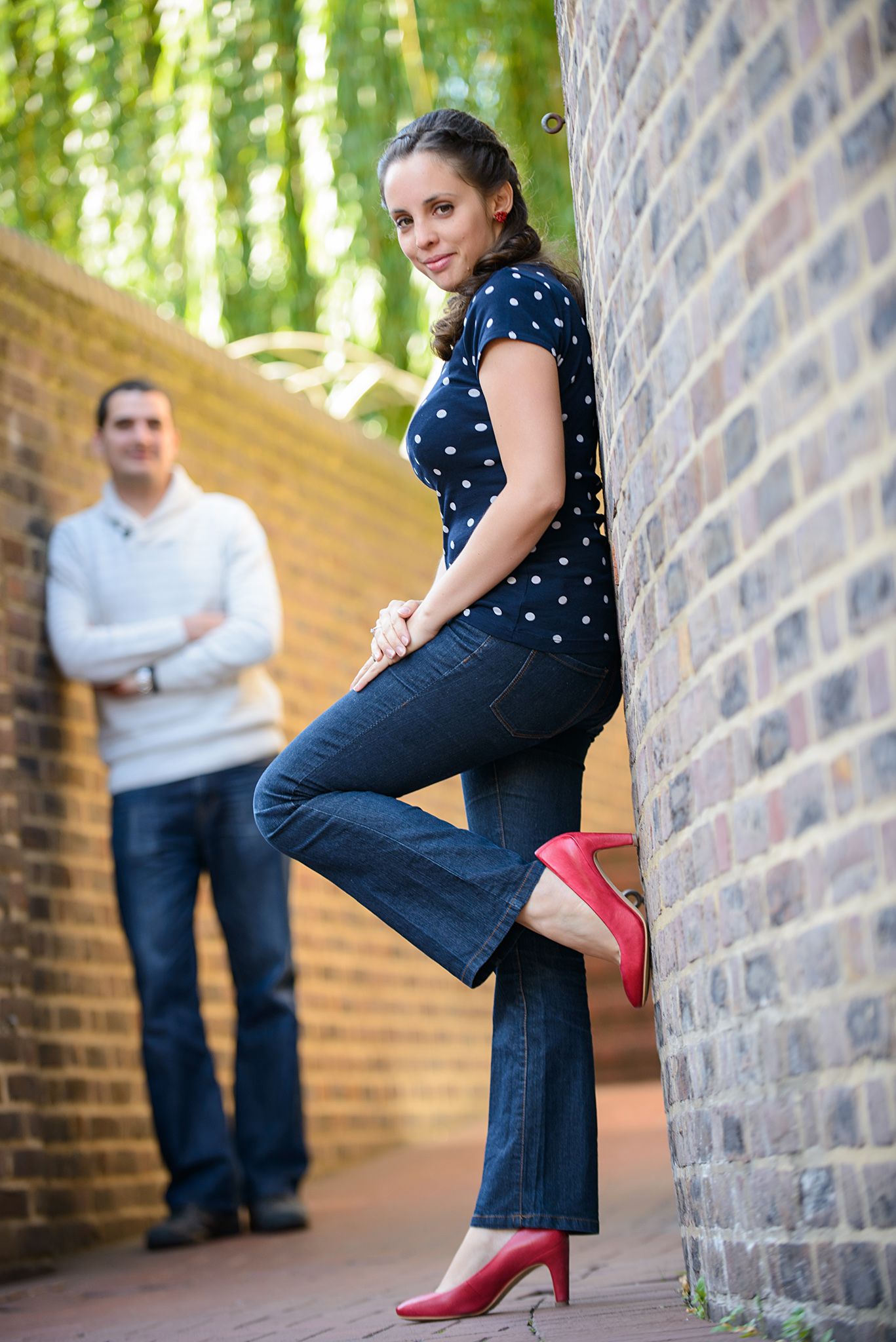 Artistic portrait showing blue polka dot dress and red heels against a brick wall backdrop.