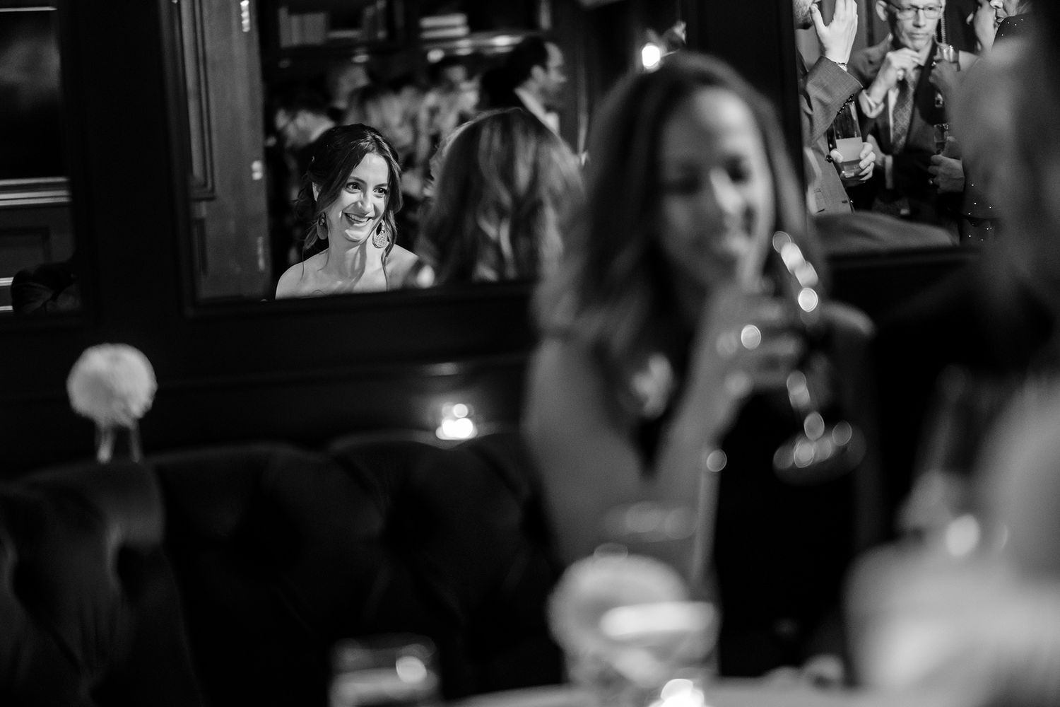 Candid black and white image of wedding reception guests mingling at tables.