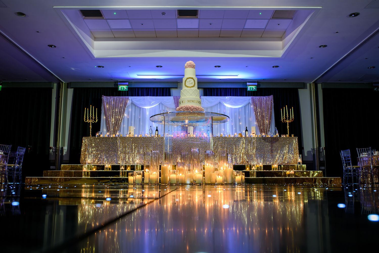 Grand ballroom with purple uplighting and glowing chandeliers set for wedding reception.
