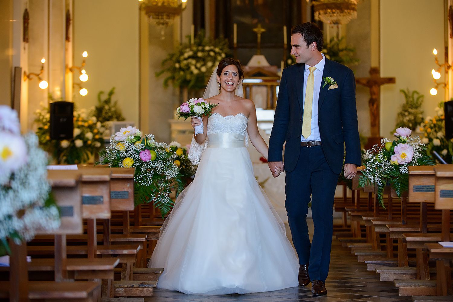 Wedding couple walking down church aisle decorated with flowers and lights.