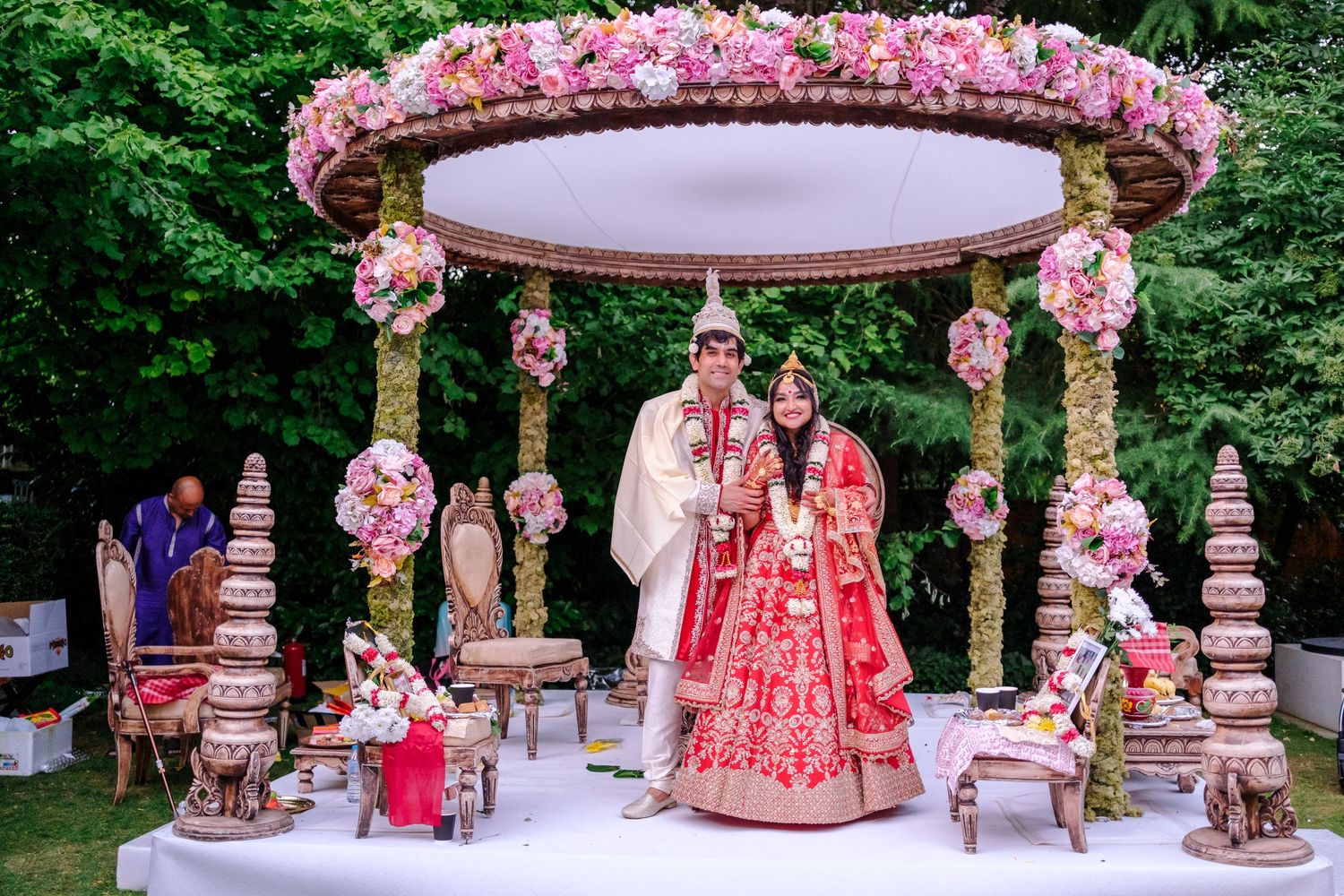 Elegant wedding dessert table decorated with pink roses and tiered cakes on ornate gold stands.