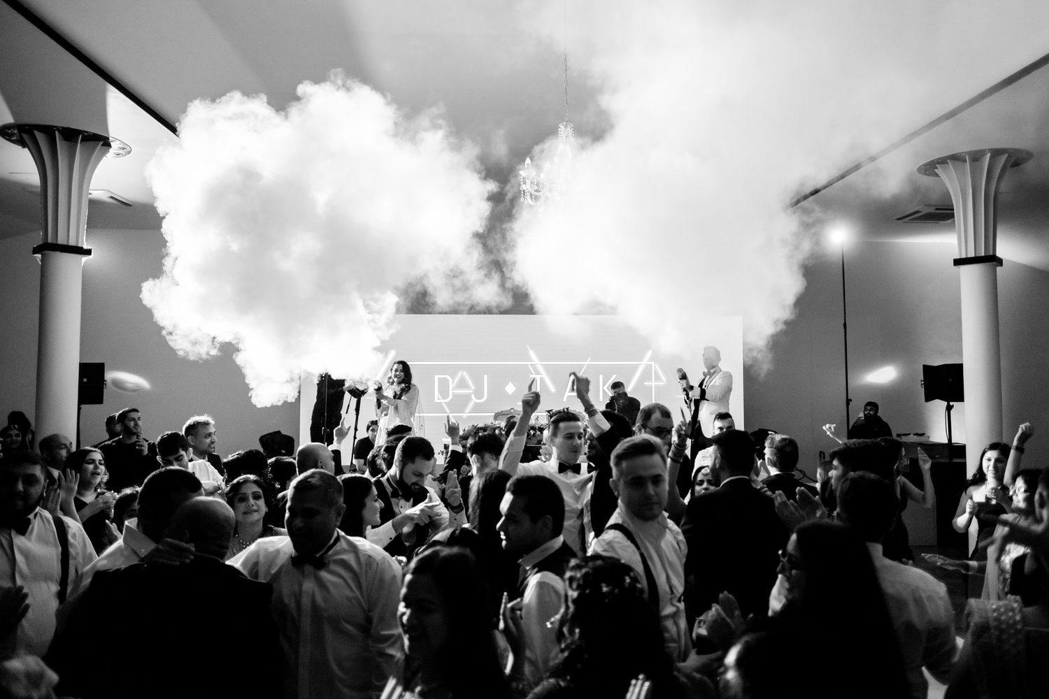 Black and white silhouette of an energetic concert crowd with raised hands against dramatic lighting.