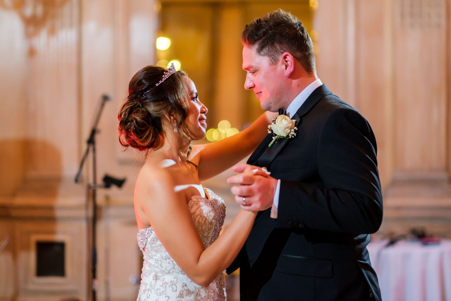 A couple shares their first dance in an elegant ballroom with warm lighting.