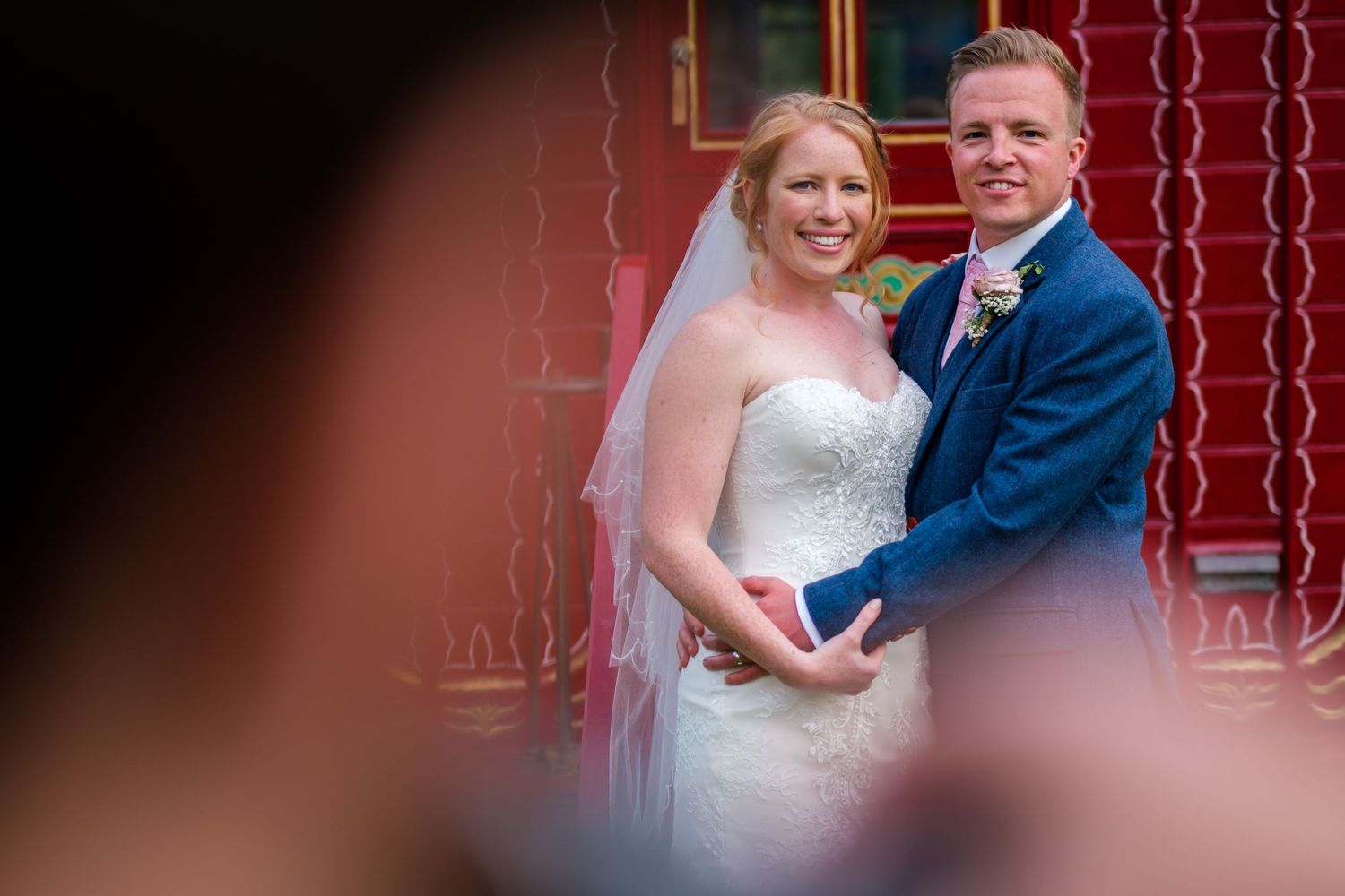 Romantic moment captured between couple at wedding with red decor background.