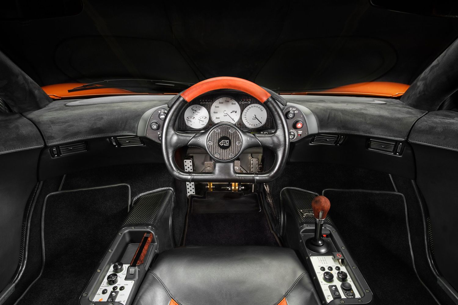 Modern sports car instrument cluster and steering wheel with red accents in dark interior.