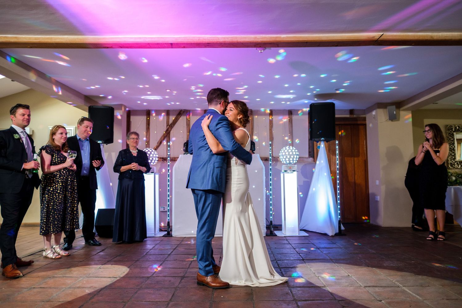 A couple shares their first dance at a wedding reception with purple and blue lighting on the dance floor.