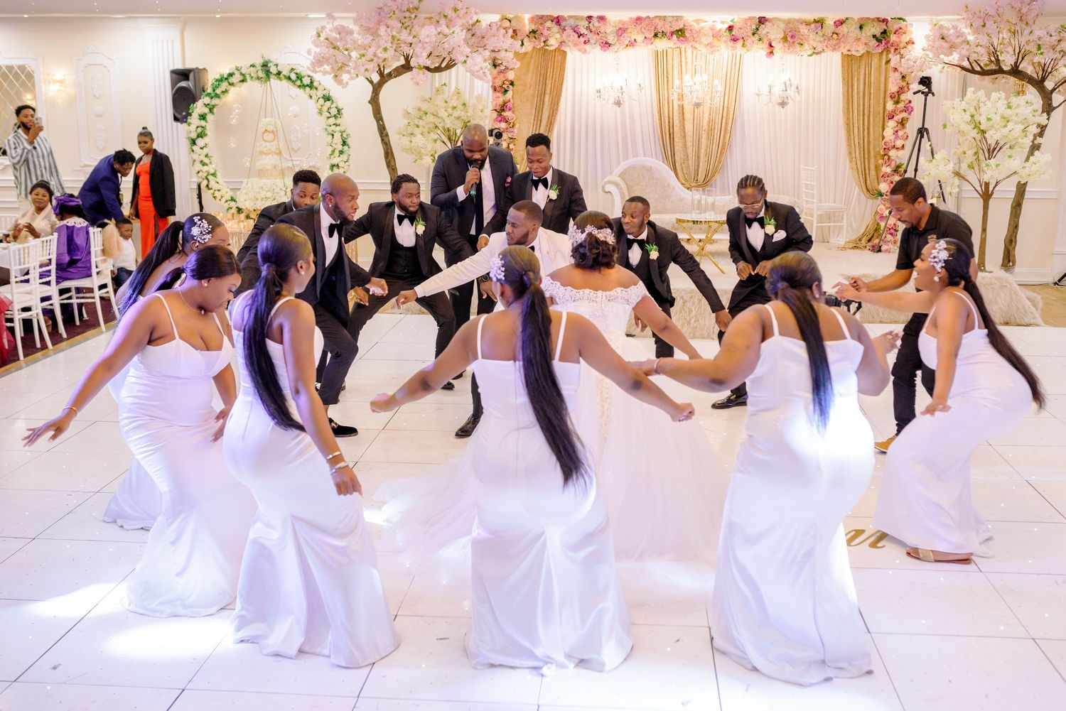Wedding party in white dresses performs choreographed dance routine in elegant reception hall.