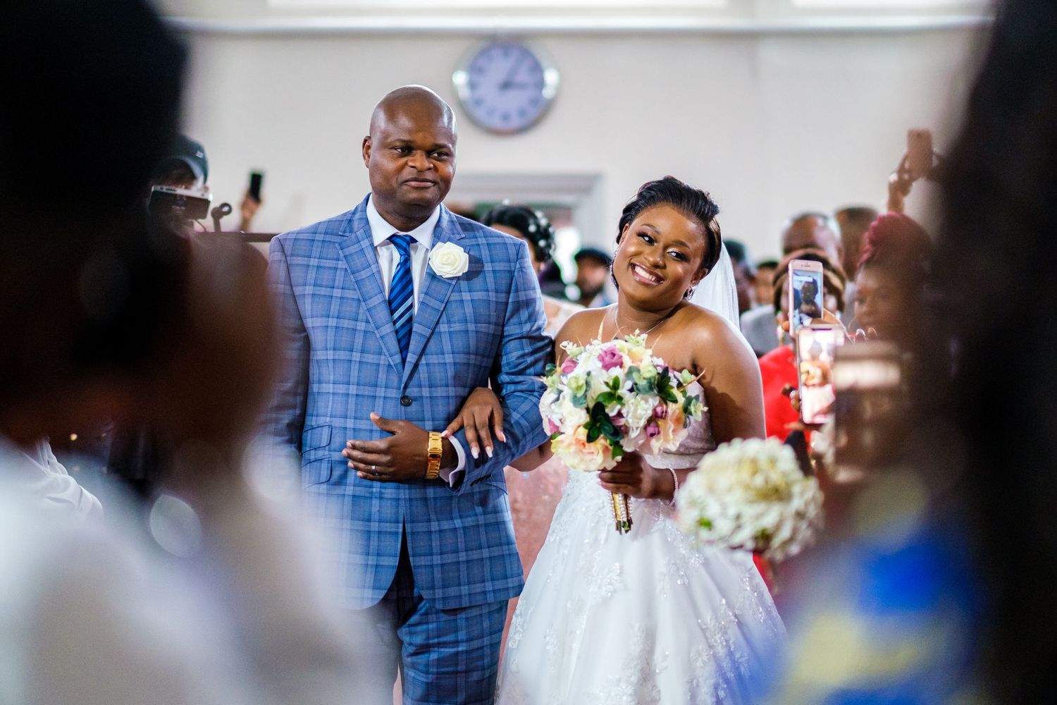 Wedding ceremony guests gather in a bright indoor venue with white walls and decor.