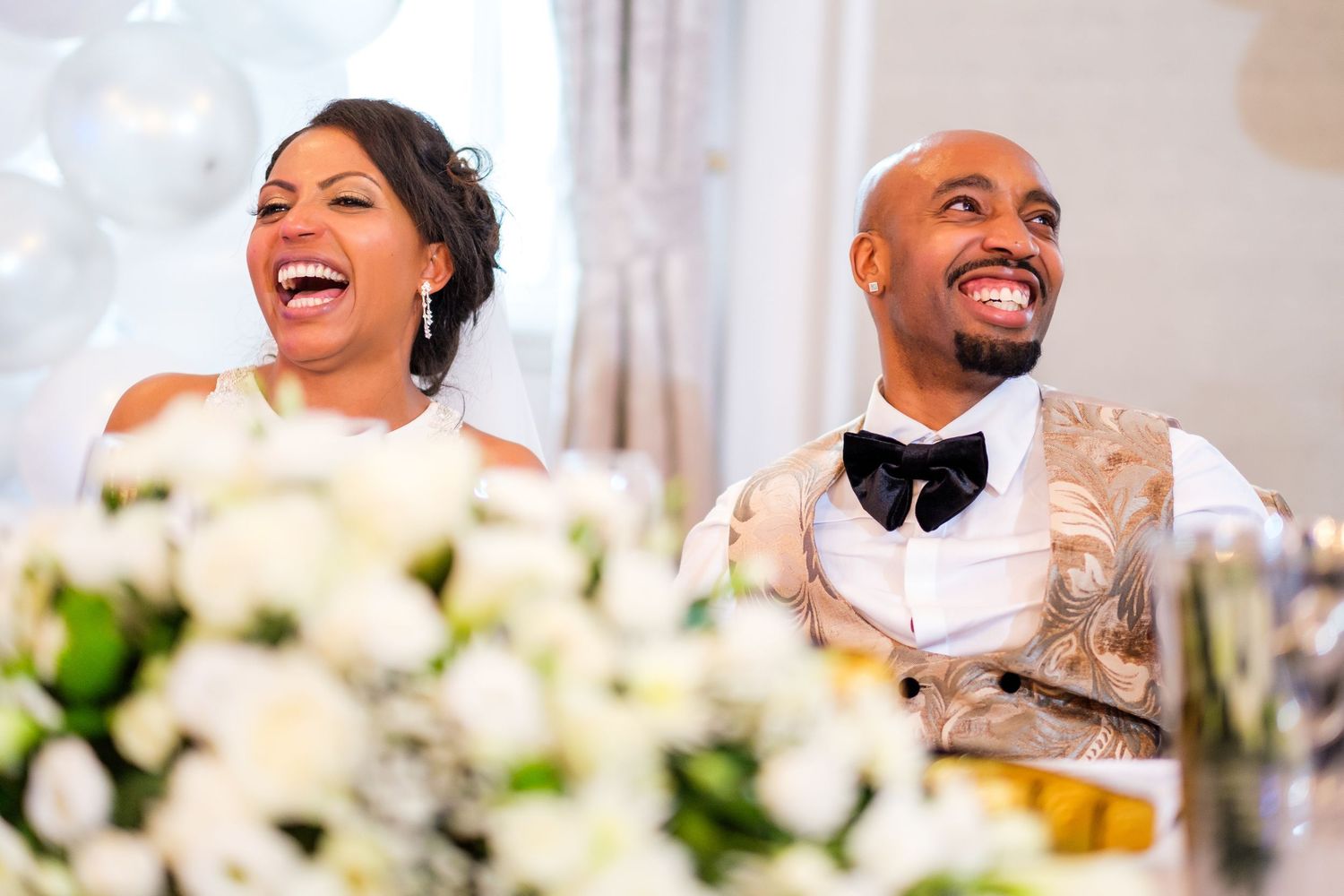 Wedding reception celebration with guests laughing and enjoying festivities in bright venue.