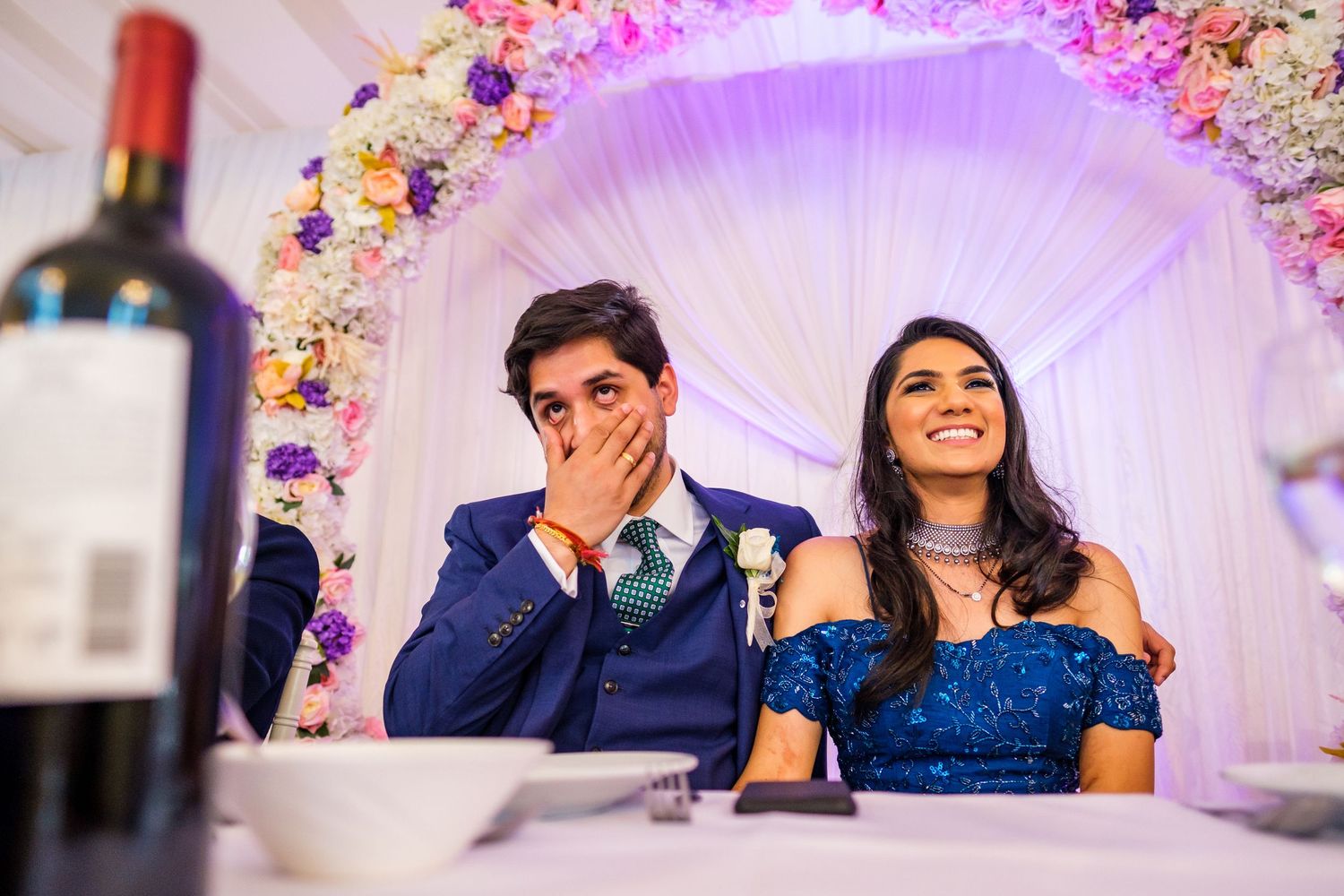Wedding reception scene with floral arch and elegant decor in soft purple lighting.