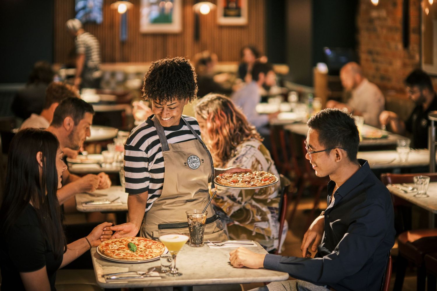 Restaurant interior showing diners enjoying meals at tables in warm ambient lighting.