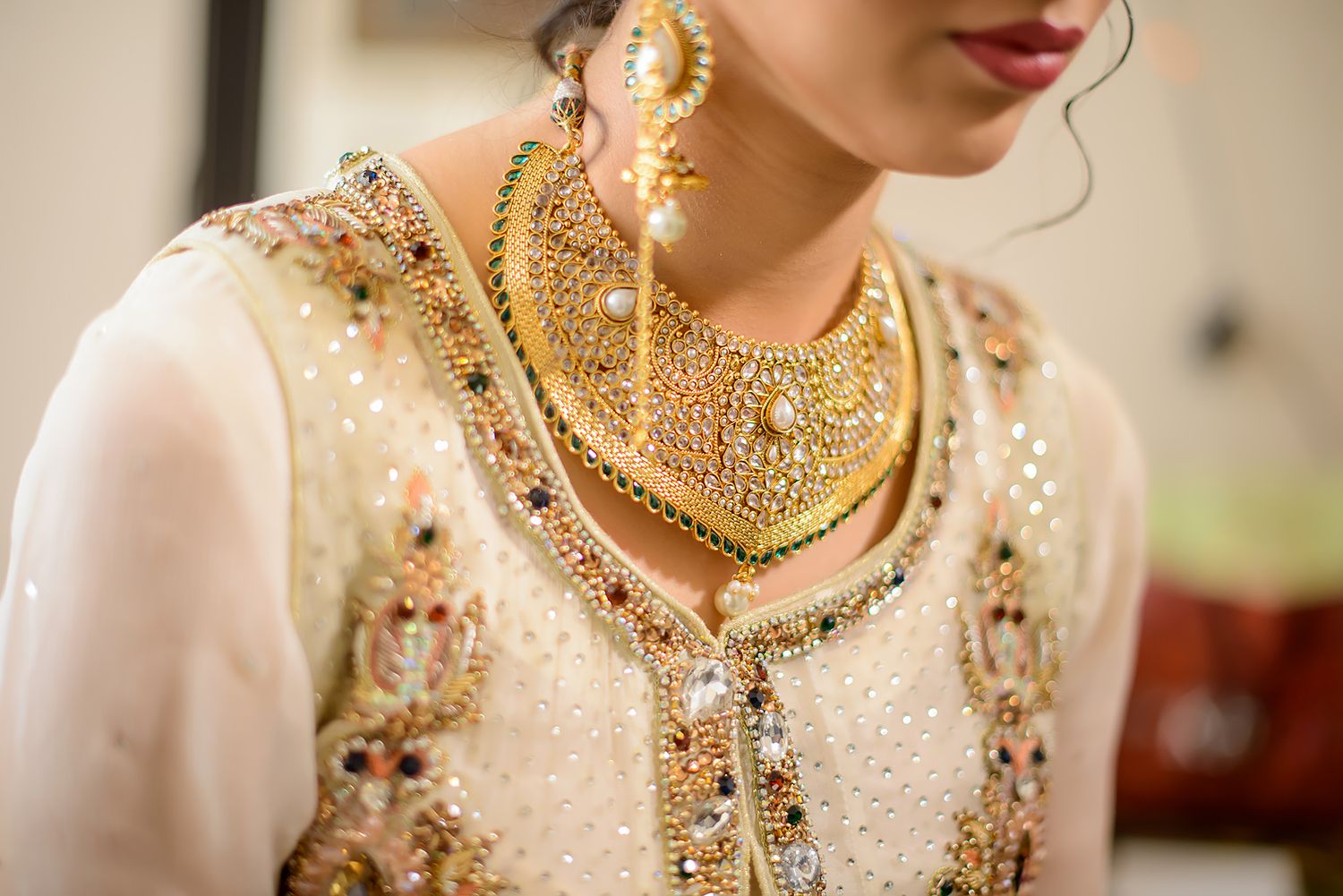 Elegant bridal details showcasing white embroidered dress and gold necklace against neutral background.