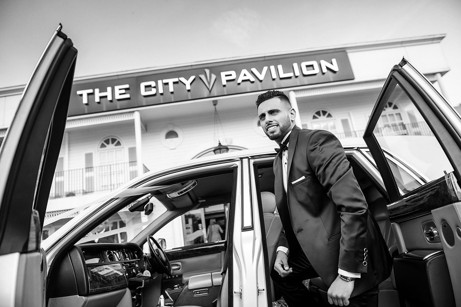 Black and white image of luxury car parked outside City Pavilion building.