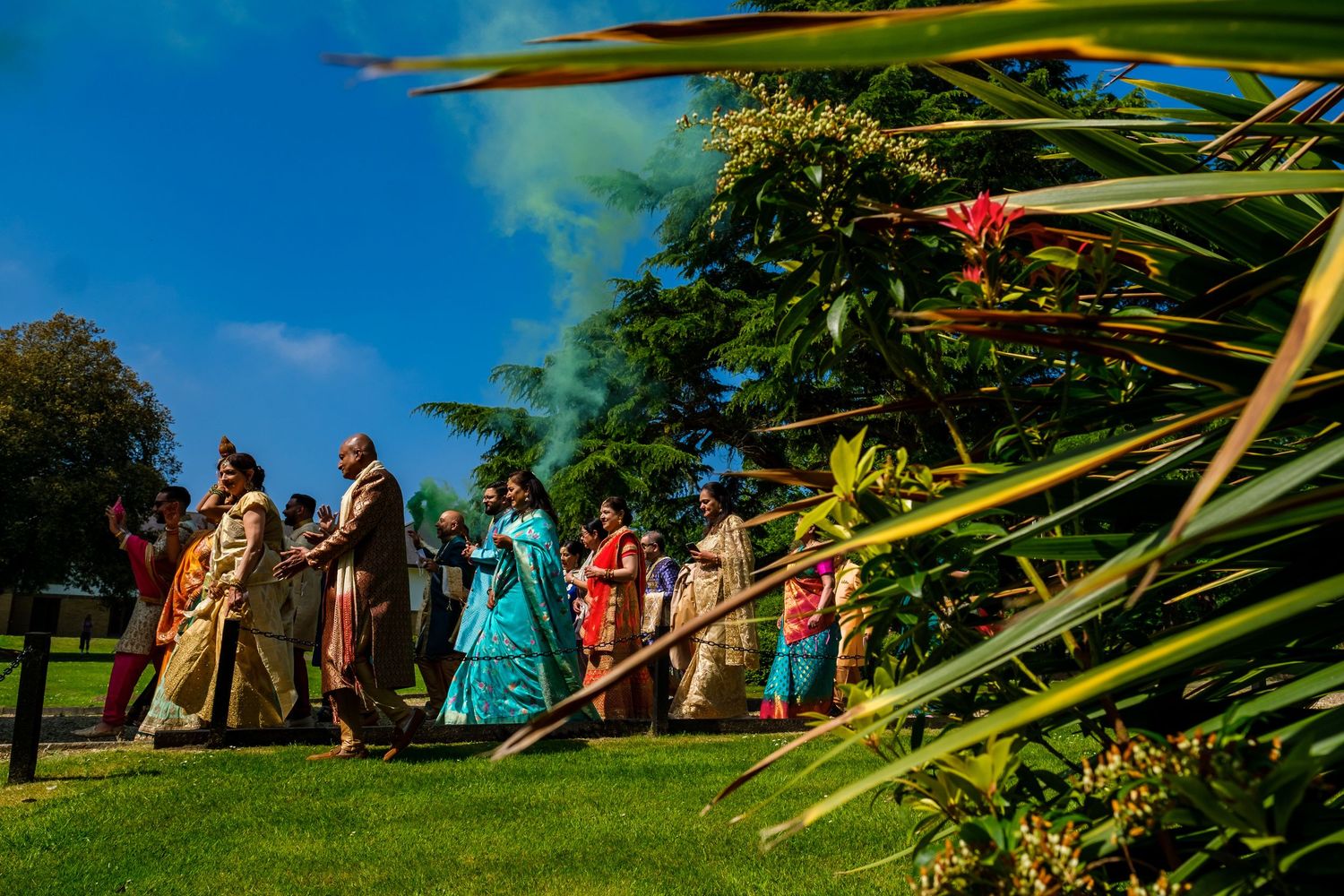 Guests in colorful traditional attire gather outdoors under palm trees for a festive celebration.