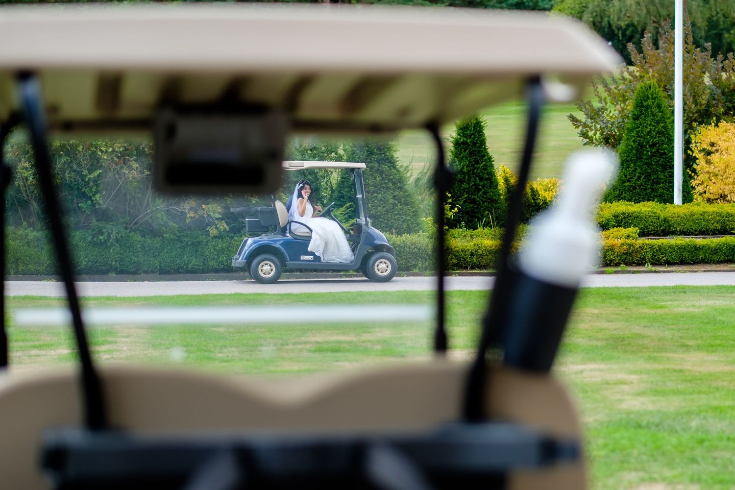 View through a golf cart windshield of another cart driving on a lush green course.