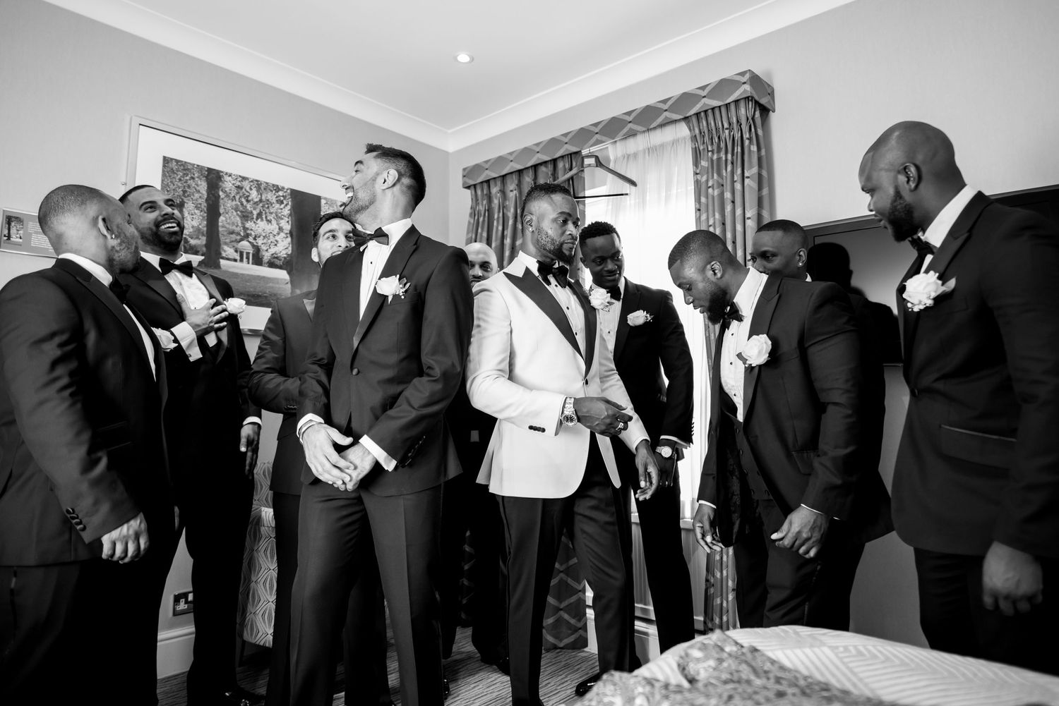 Black and white candid shot of groomsmen sharing a lighthearted moment during wedding preparations.