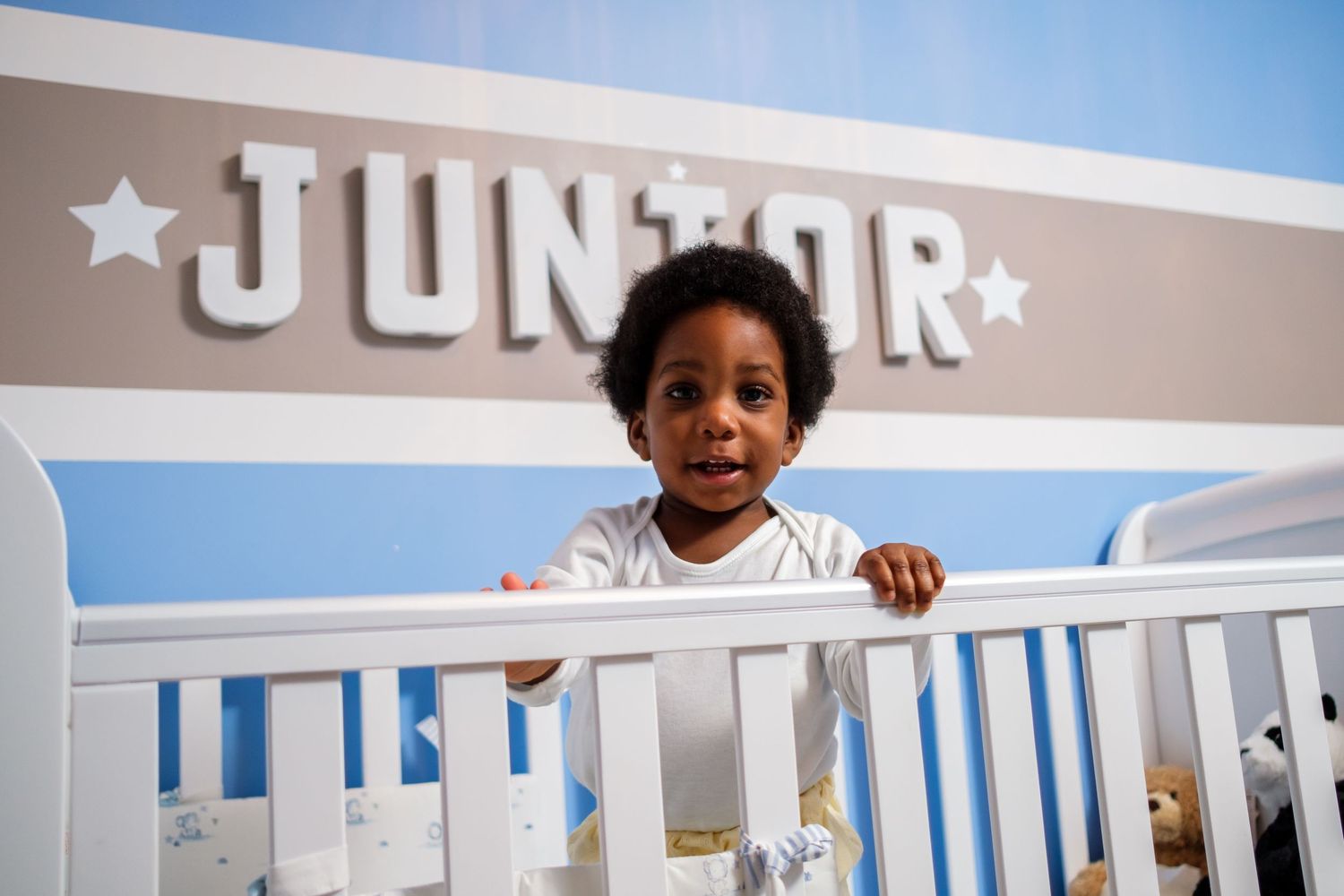 Baby's white nursery with crib rails and star decor against pastel blue walls.