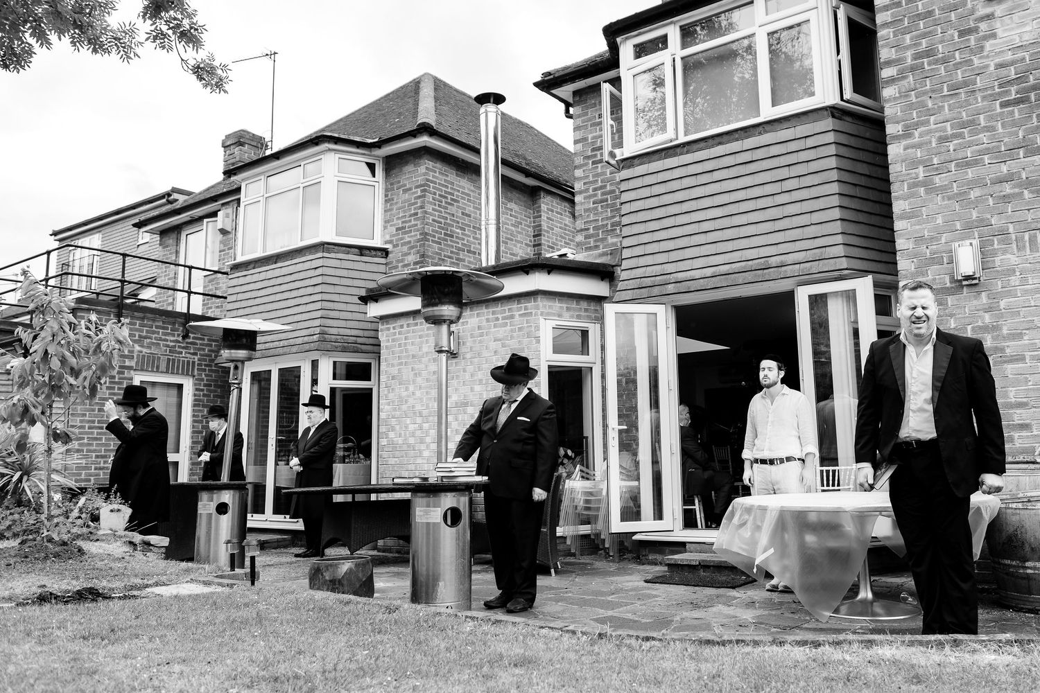 Multiple exterior black and white photos show figures in dark coats in front of residential brick buildings.