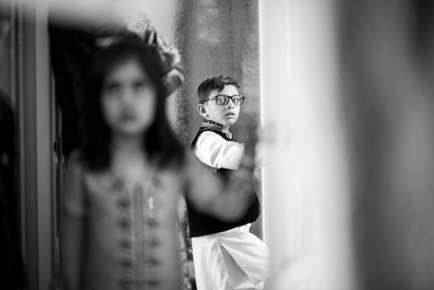 Artistic black and white portrait through window columns creating shadow effects.