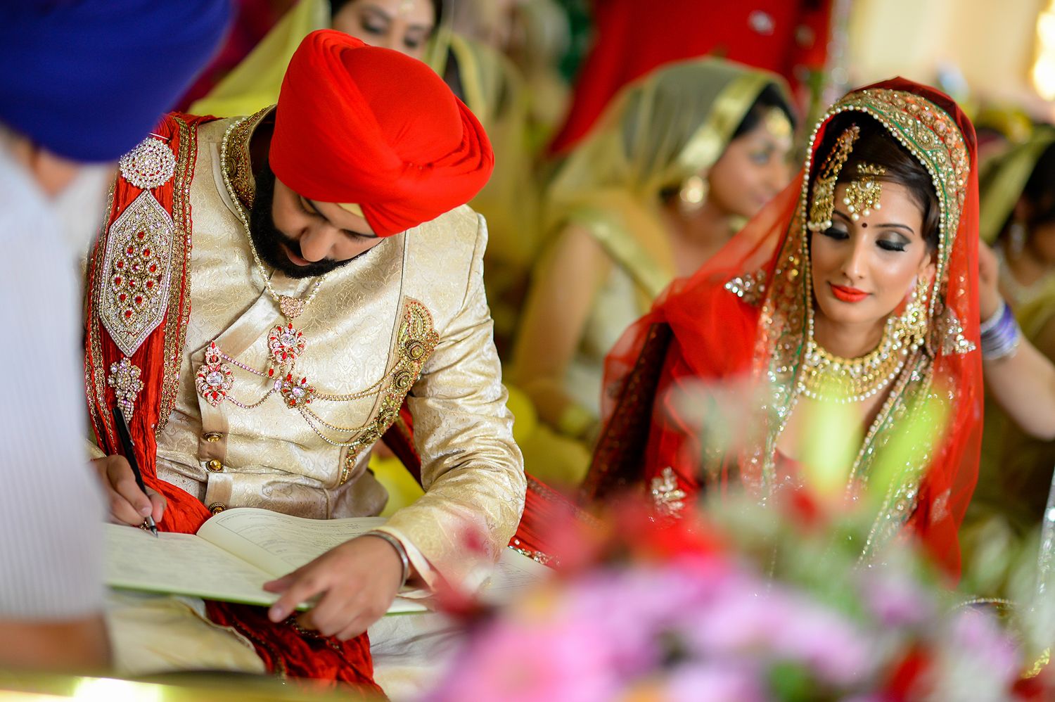 Traditional Sikh wedding ceremony with bride and groom signing documents in ornate attire.