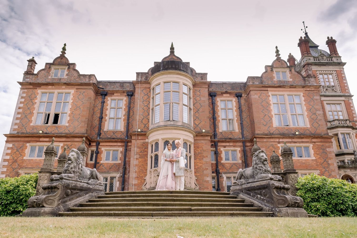 Historic red brick mansion with ornate Victorian architecture and stone statues along its facade.