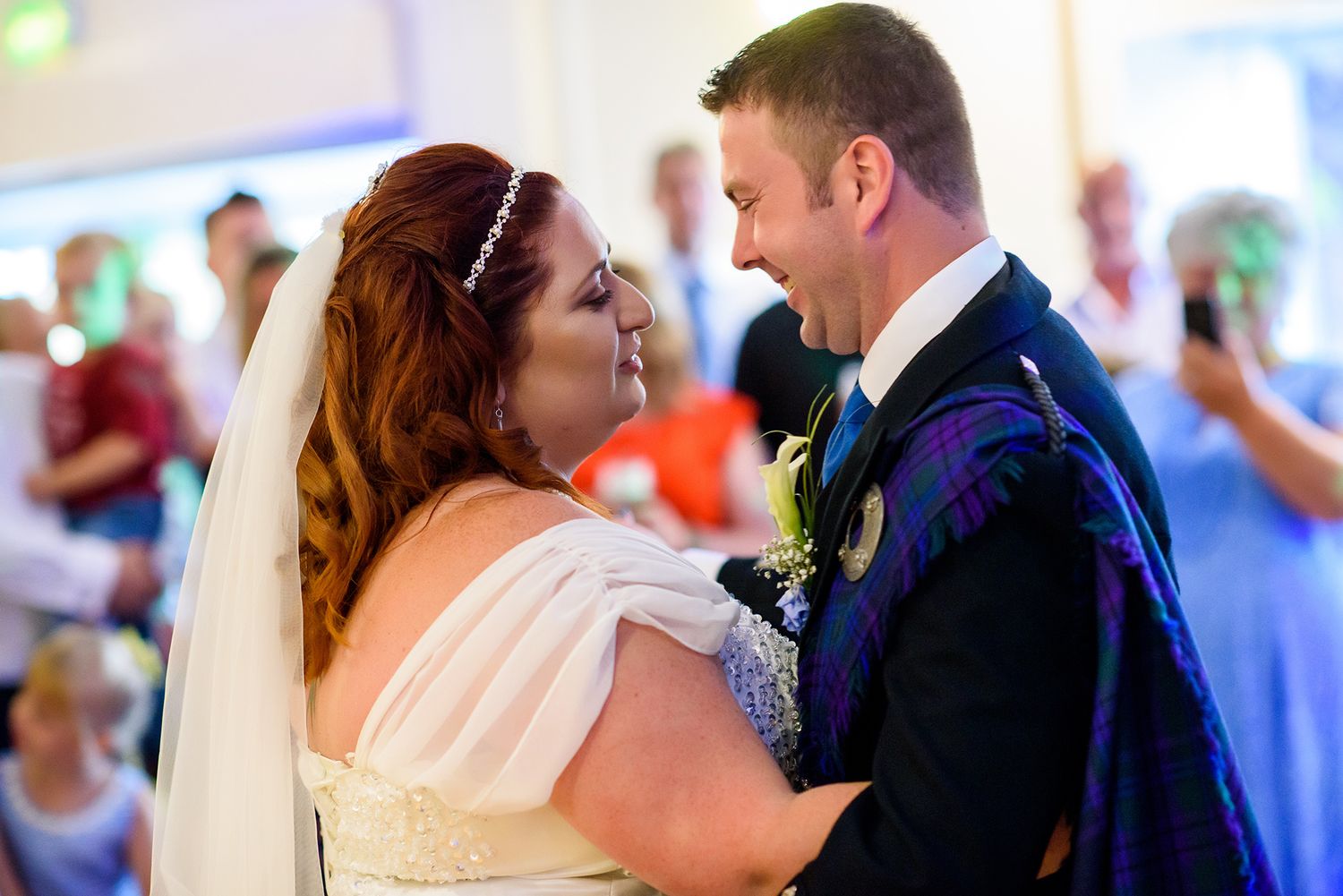 Couple sharing their first dance at wedding reception with guests watching in background.