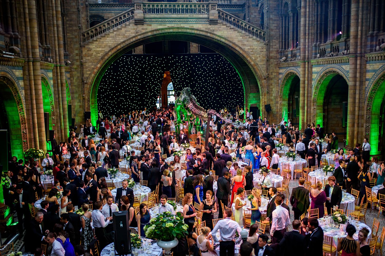 Elegant banquet dinner setup under gothic arches with dramatic green lighting.