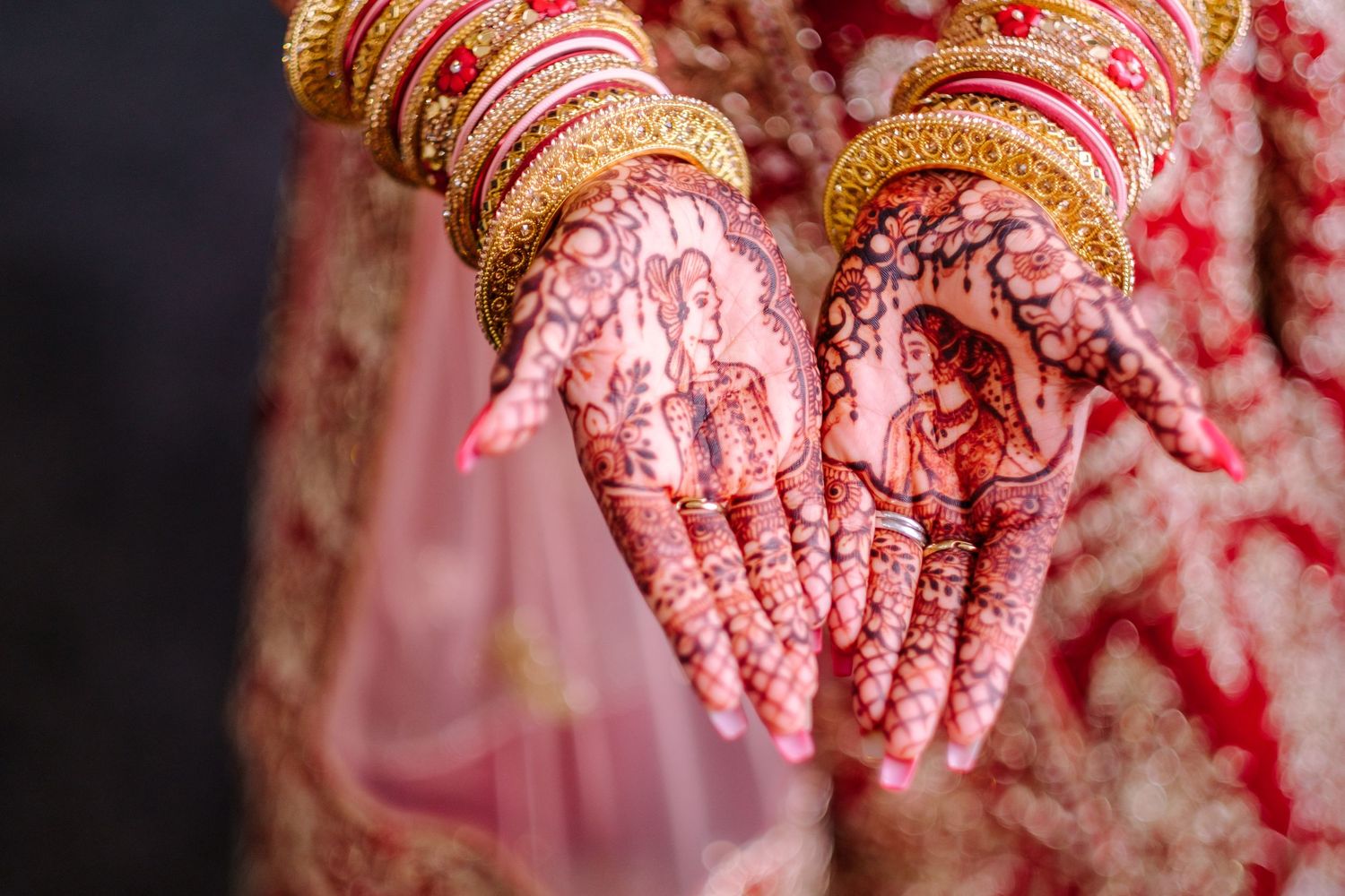 Traditional henna adorned hands with bangles showcase intricate mehndi designs at an Indian wedding ceremony.