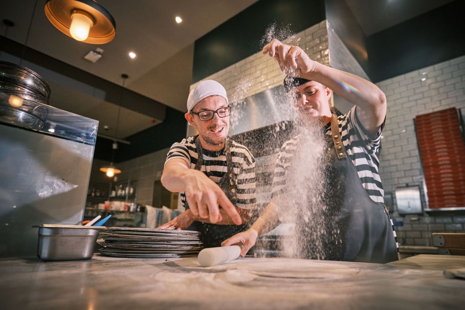 Chef preparing food in professional kitchen with flour dusting in dramatic lighting.