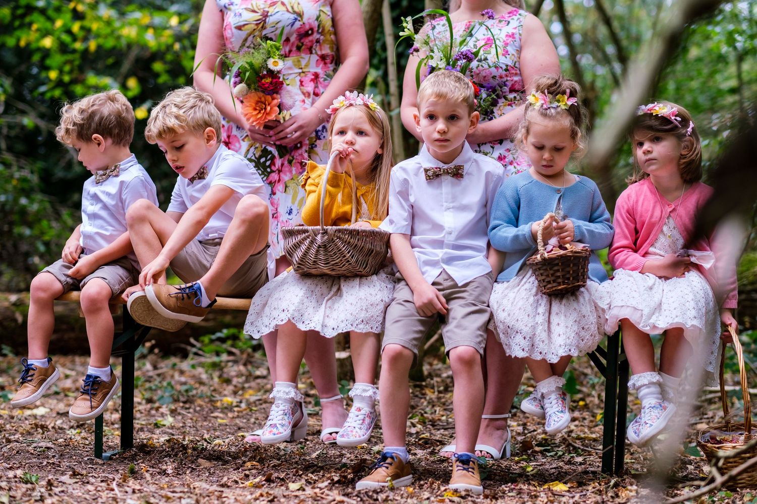 Children sitting on wooden benches in an outdoor garden setting during a wedding celebration.