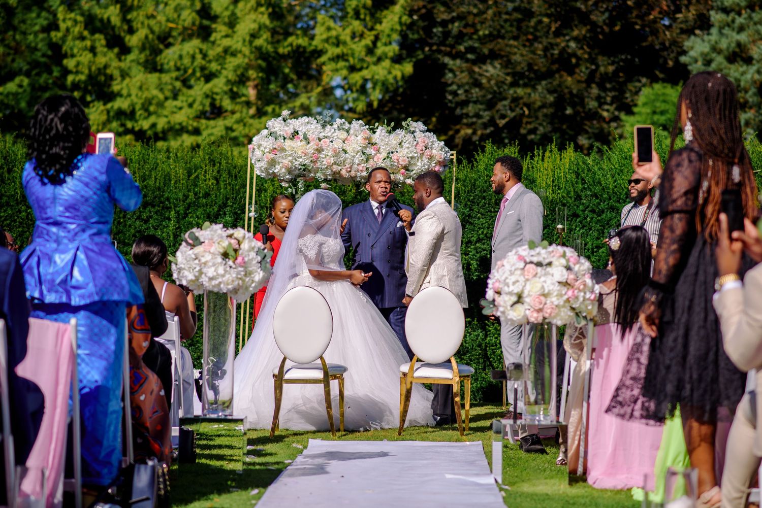 Outdoor garden wedding ceremony setup with pink floral arrangements and white chairs.