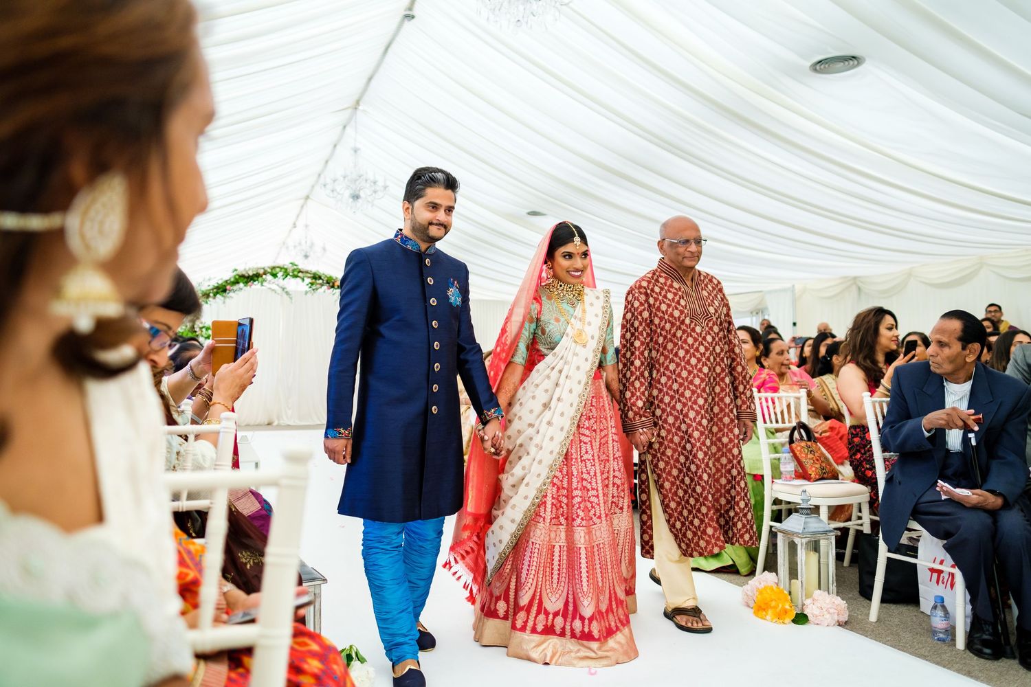 Wedding reception under white tent with guests seated at decorated tables.