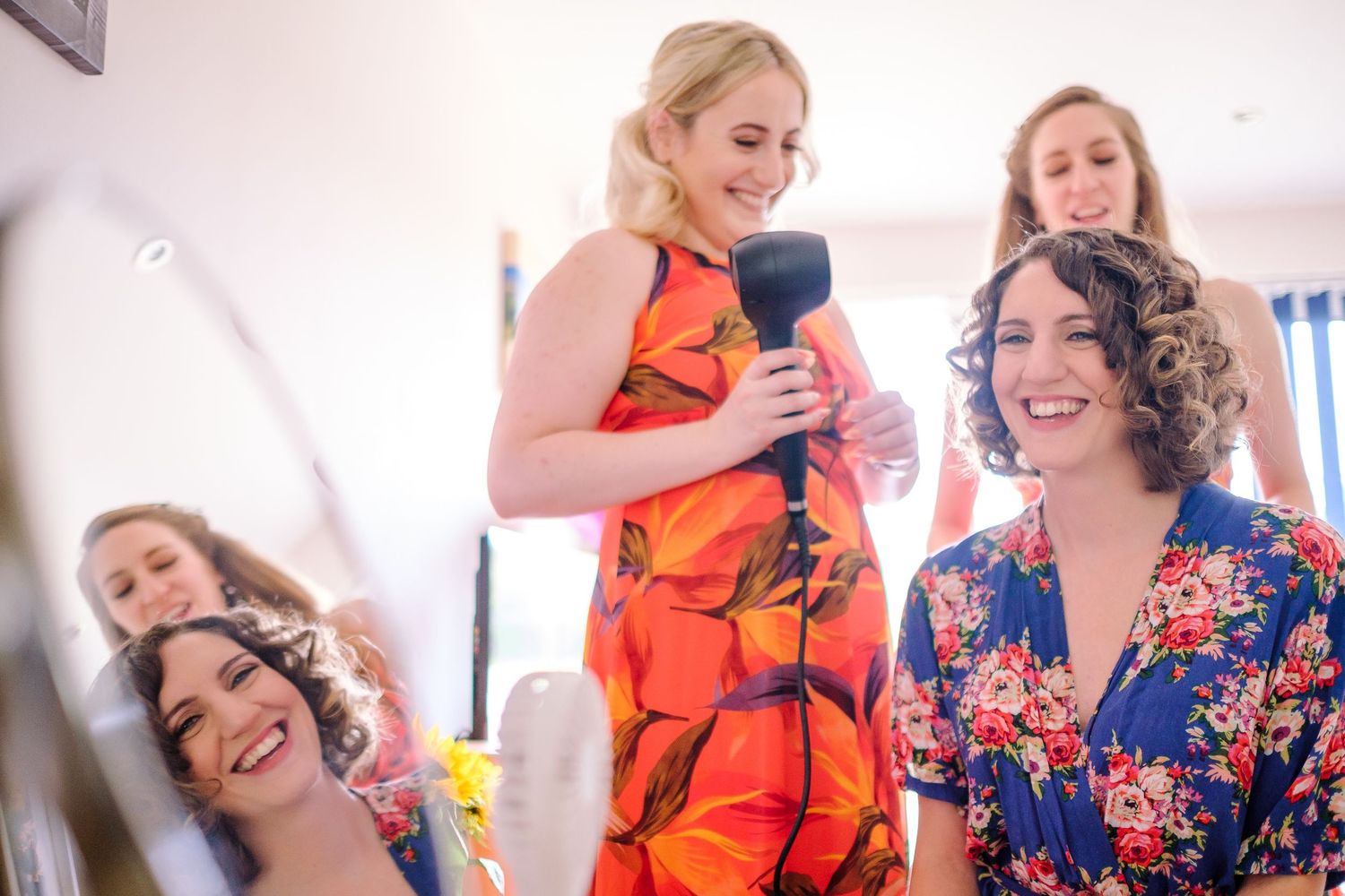 A group of women wearing colorful floral and orange dresses gather together in a bright indoor setting.