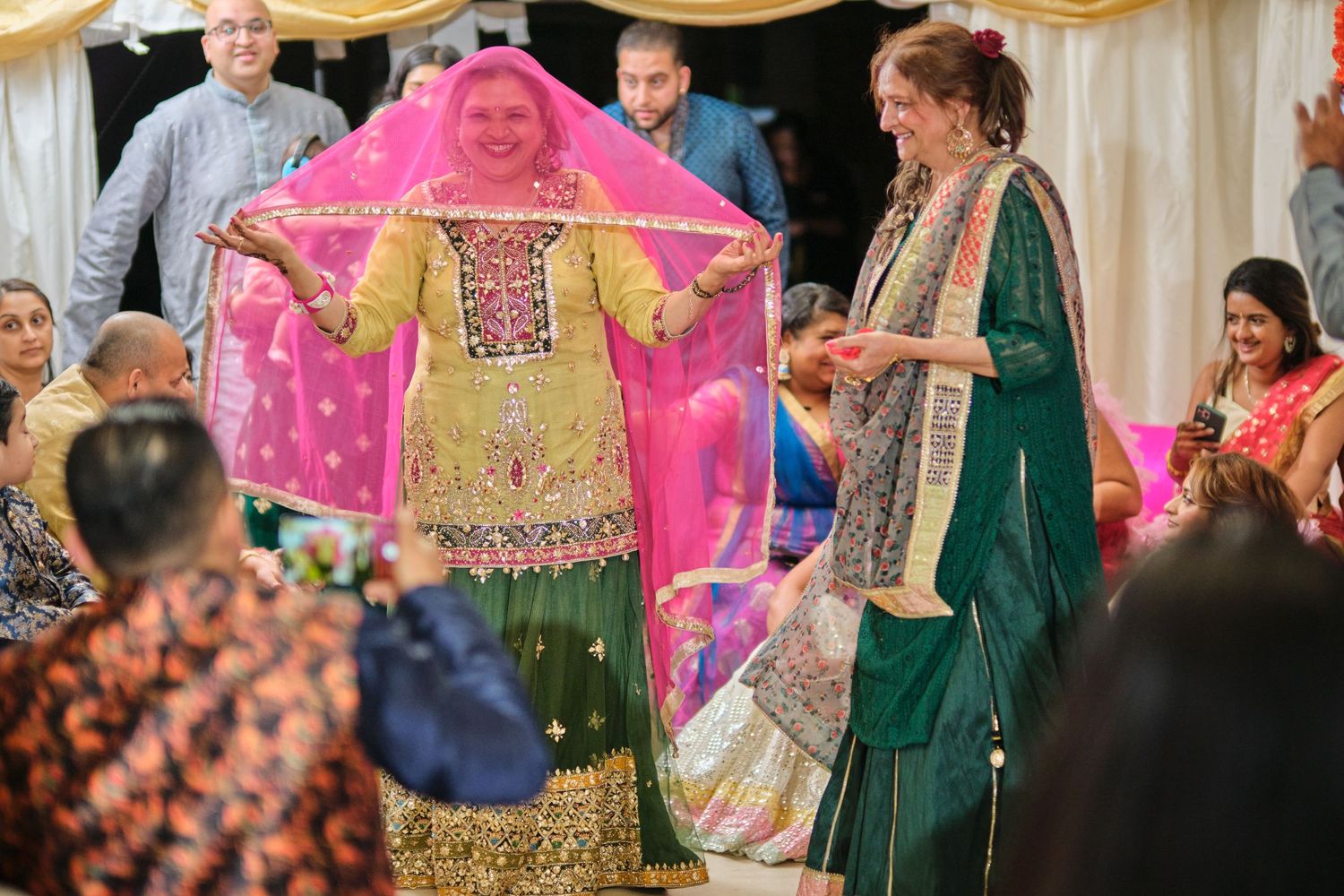 Wedding celebration with guests in vibrant outfits and decorative pink umbrella.