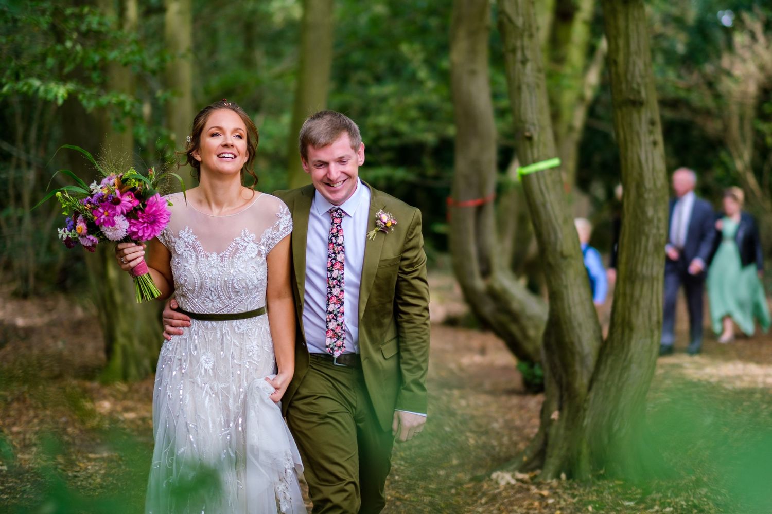 Wedding party walking through a green wooded area on a sunny day.
