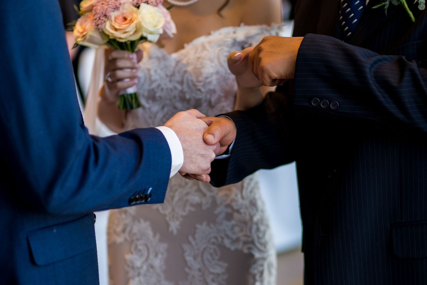 Close-up of two people in formal attire shaking hands during a wedding ceremony.
