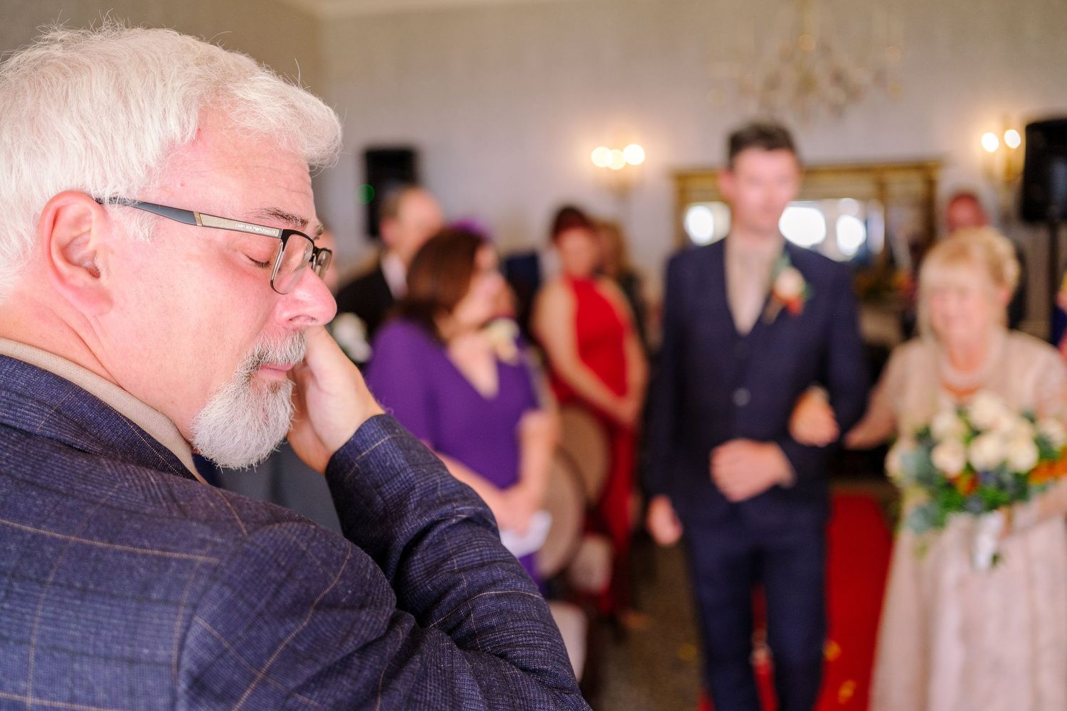 An emotional moment captured during a wedding ceremony as guests look on in a softly lit indoor venue.