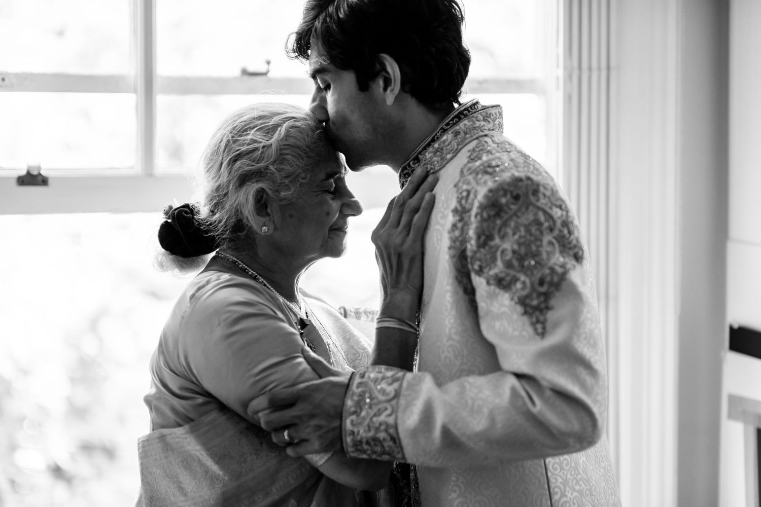 A tender black and white moment captured between two people in an intimate embrace by a window.