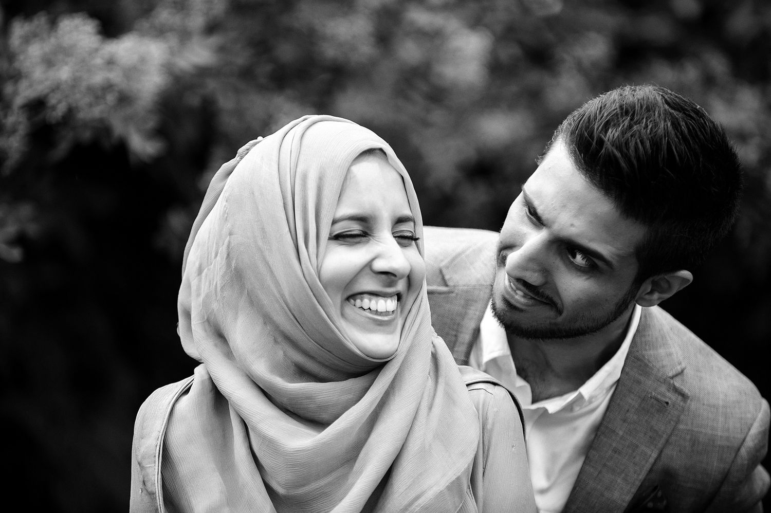 Black and white candid portrait of a couple laughing and embracing outdoors on their wedding day.