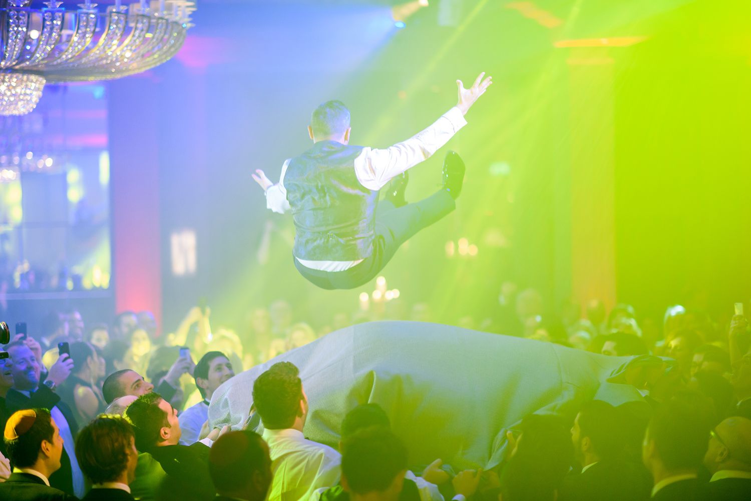 Aerial performers soar above a crowded nightclub with colorful green and blue lighting effects illuminating the scene.