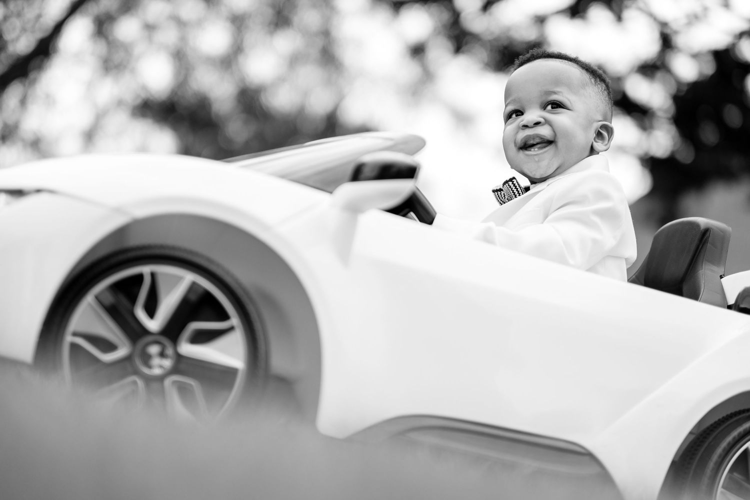 Children enjoying a sunny day riding in a white toy car, captured in black and white photography.