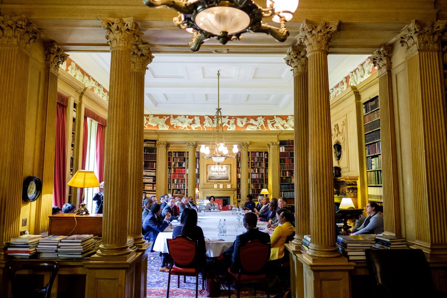 Grand historic dining room with classical columns and elegant furnishings in golden tones.