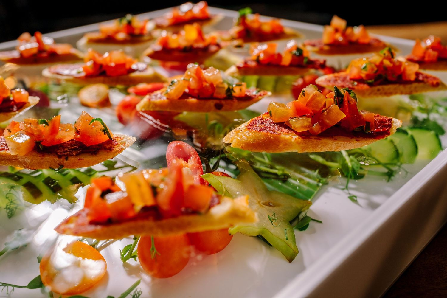 Vibrant orange shrimp appetizers served on fresh greens arranged in rows on a white serving platter.