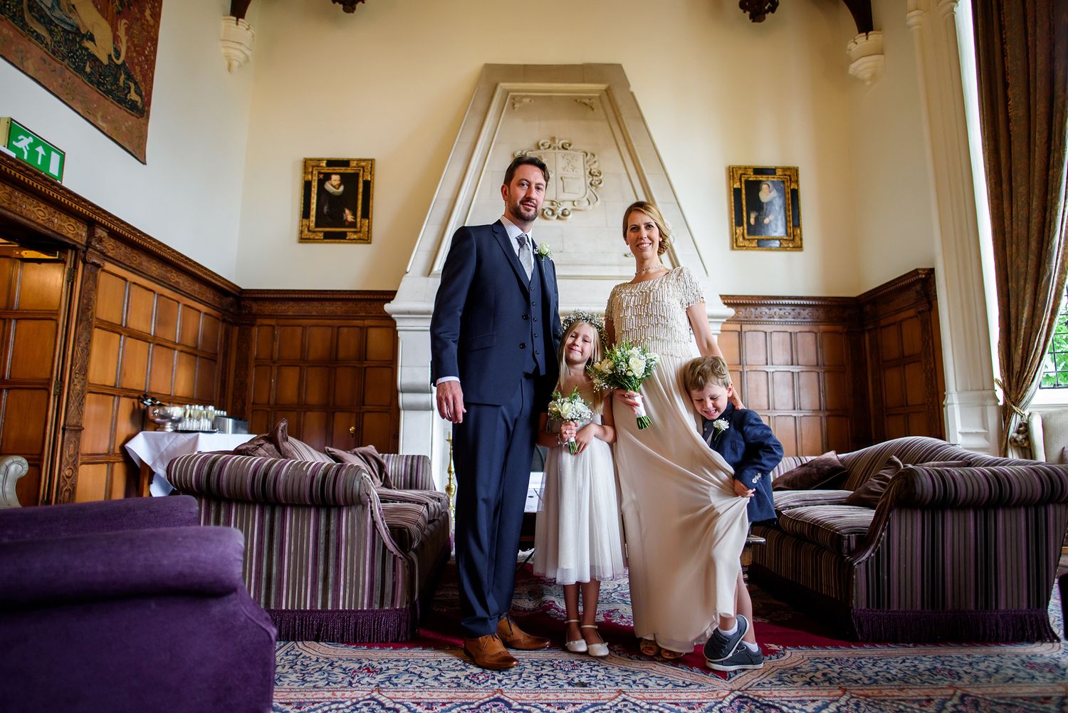 Elegant wedding party poses in a grand room with wood-paneled walls and purple furnishings.