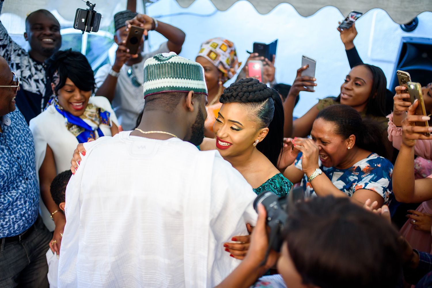Celebratory crowd gathered under white tent canopy during festive event.