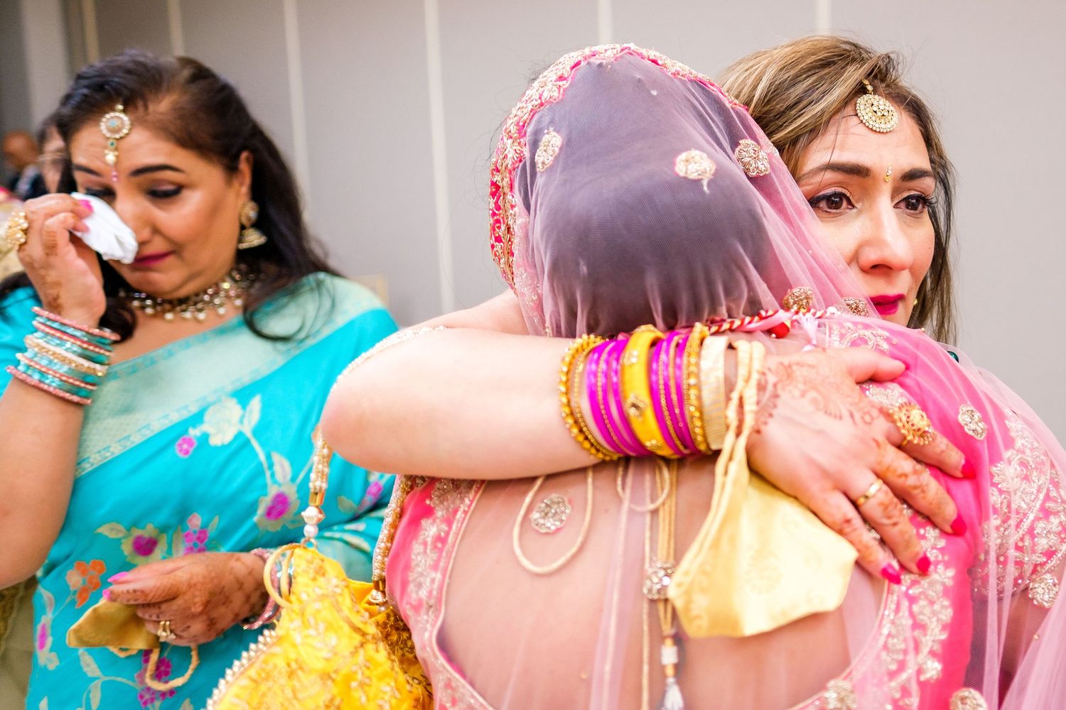 Wedding guests share emotional hugs and embraces during a traditional Indian celebration while wearing colorful sarees.
